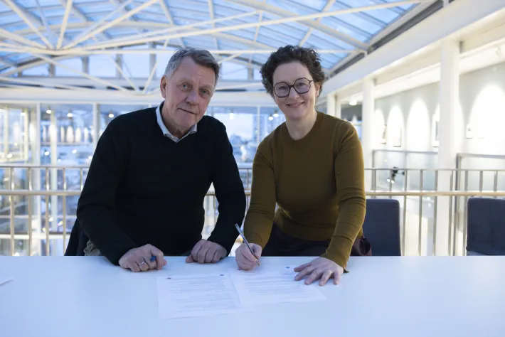 Ordf&oslash;rer og NAVs regiondirekt&oslash;r undertegner papir. Smiler mot kamera.