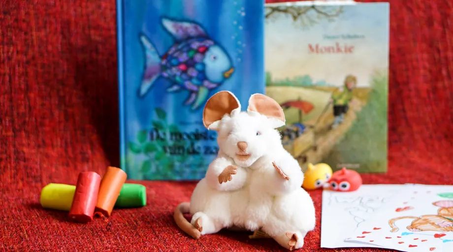 Barnebok, musebamse, tegnestifter og tegneark p&aring; r&oslash;d duk.