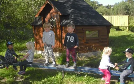 Bjerkaker barnehage uteområdet Bjerkaker barnehage uteområde med lekehus og seks barn på en huske en sommerdag med grønt gress