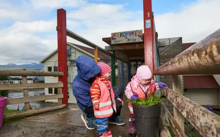 Reinen barnehage inngangsparti Reinen barnehage inngang med tre barn som ser på blomster i en krukke en våt sommerdag