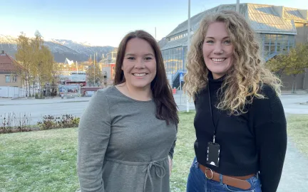 Sigrid Mog&aring;rd-Jansen, til venstre, og Helga B&aring;rdsdatter Kristiansen fra Troms&oslash; kommune st&aring;r p&aring; plenen utenfor r&aring;dhuset, og smiler mot kamera.
