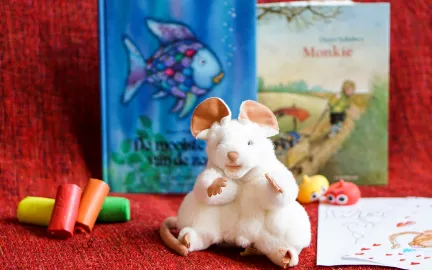 Barnebok, musebamse, tegnestifter og tegneark p&aring; r&oslash;d duk.