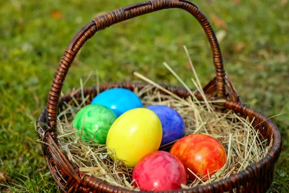 Egg malt i ulike farger ligger i en brun kurv. Gr&oslash;nt gress i bakgrunnen. Foto.