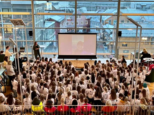 En stor gruppe jenter sitter på plan 2 i biblioteket med ryggen vendt mot kameraet. Foto. Girl Tech Fest 2022