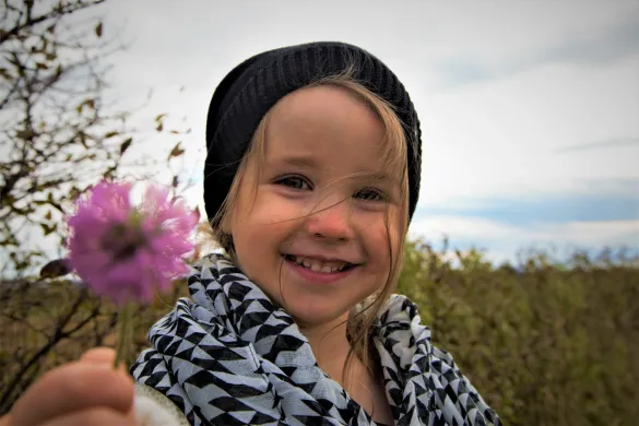 Smilende jente som holder en blomst i h&aring;nden