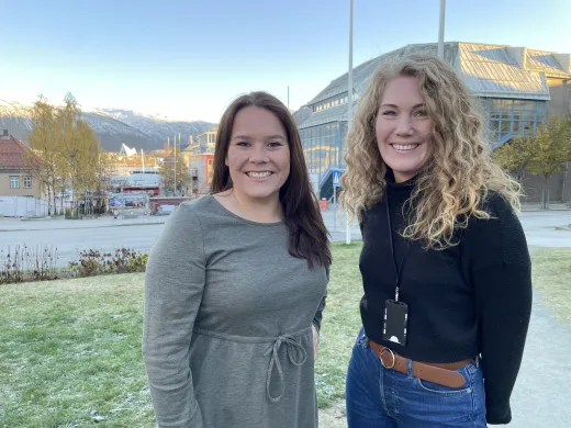 Sigrid Mog&aring;rd-Jansen, til venstre, og Helga B&aring;rdsdatter Kristiansen fra Troms&oslash; kommune st&aring;r p&aring; plenen utenfor r&aring;dhuset, og smiler mot kamera.
