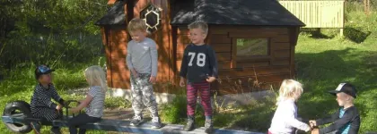 Bjerkaker barnehage uteomr&aring;de med lekehus og seks barn p&aring; en huske en sommerdag med gr&oslash;nt gress