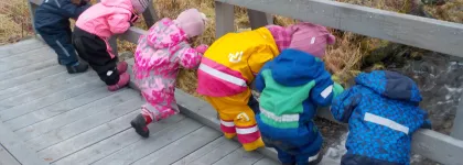 Seks barn som st&aring;r p&aring; en bro og ser ned i elva ved Kattfjord barnehage