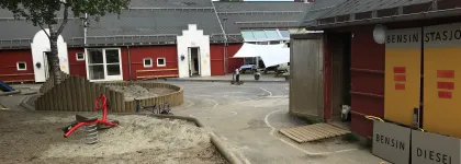 Olsg&aring;rd barnehage uteomr&aring;de med et stort tre, sandkasser og lekeapparater en sommerdag
