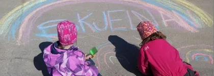 To barn tegner regnbue med kritt i barnehagens uteomr&aring;de en solrik sommerdag