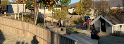 Gimle studentbarnehage med lekeomr&aring;de sett utenfra en sommerdag med bl&aring; himmel